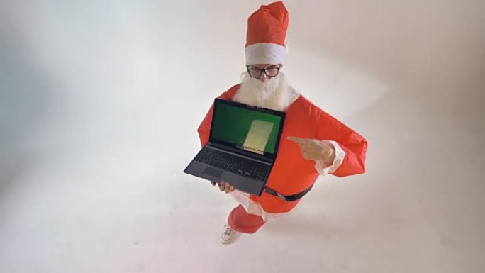 穿着充气服的圣诞老人指向带有绿色屏幕的礼品笔记本电脑。