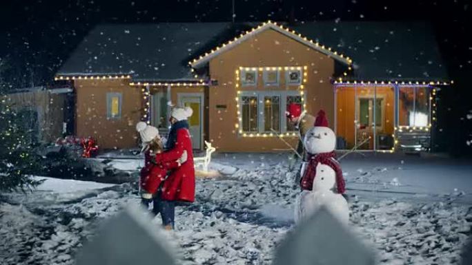 在快乐的冬天晚上，年轻的父亲，母亲和可爱的小女儿在雪球中玩耍，在他们用花环装饰的田园诗般的房子的后院