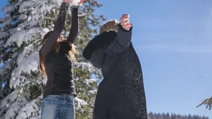两个女人在雪地里跳舞和玩耍，像下雪一样向空中扔雪