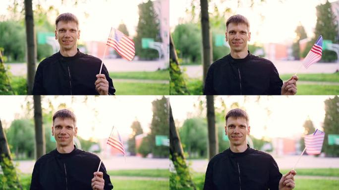 美国男子挥舞着美国国旗，微笑着看着相机的慢动作肖像。年轻人，快乐的公民，国家和城市的概念。