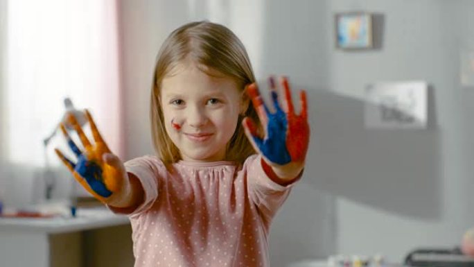 可爱的微笑女孩展示她的双手被彩色油漆覆盖。