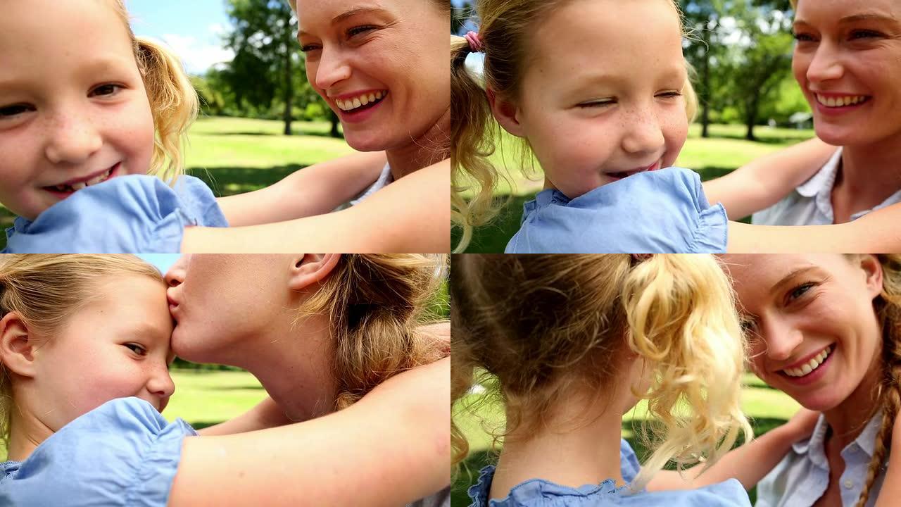 快乐的母亲在公园亲吻她的小女孩