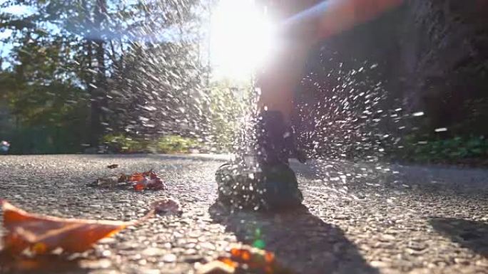 慢动作，镜头耀斑: 湿徒步运动鞋撞到沥青时，水会飞溅。