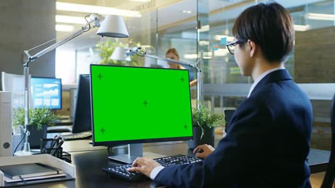 在办公室里，商人在带有模拟绿屏的台式个人计算机上工作。同事进入办公室，在她的办公桌前进行。