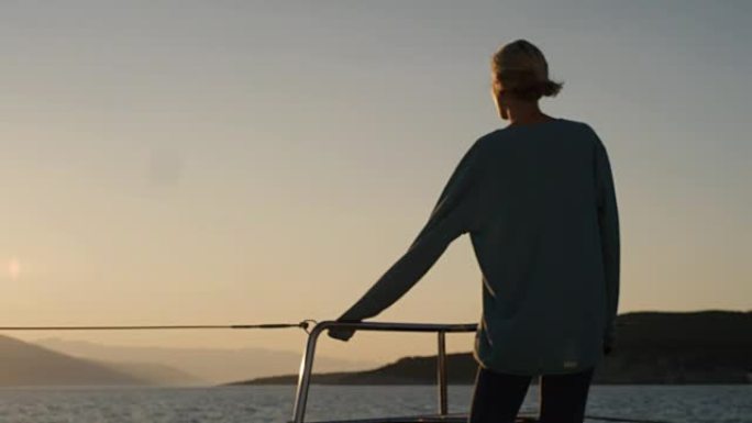 美丽的年轻女子在游艇的甲板上散步，戴上墨镜，欣赏带海景的日落。