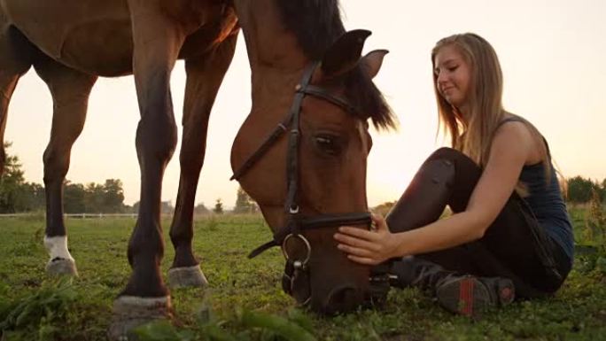 特写: 女孩坐在牧场上的地面上，旁边是一匹放牧的马