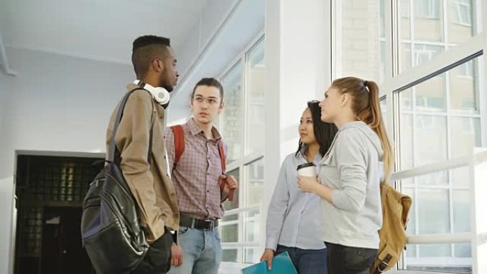 四个多种族的学生正站在大学的白色宽敞大厅里，以积极的方式互相交谈。他们积极地笑着
