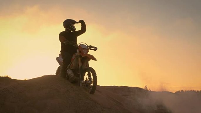 专业的越野摩托车手在他的耐久摩托车上壮观地站在越野沙丘上。在整个赛道上看得很远。