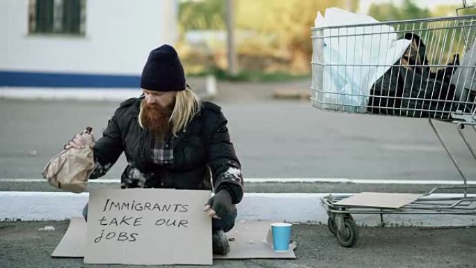 由于欧洲的移民危机，愤怒的年轻无家可归的人坐在购物车附近，在寒冷的日子里喝酒