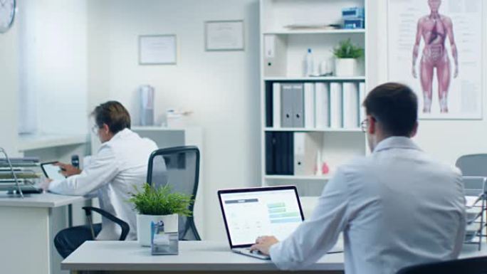 男医生在笔记本电脑上读取患者的医疗卡并进行更正，他的助手在后台工作。办公室现代、宽敞、轻便。