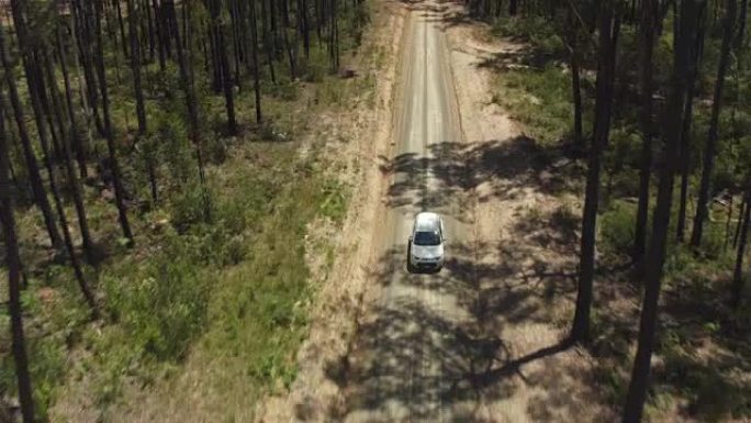 空中: 白色SUV汽车沿着泥泞的道路行驶，穿过茂密的森林
