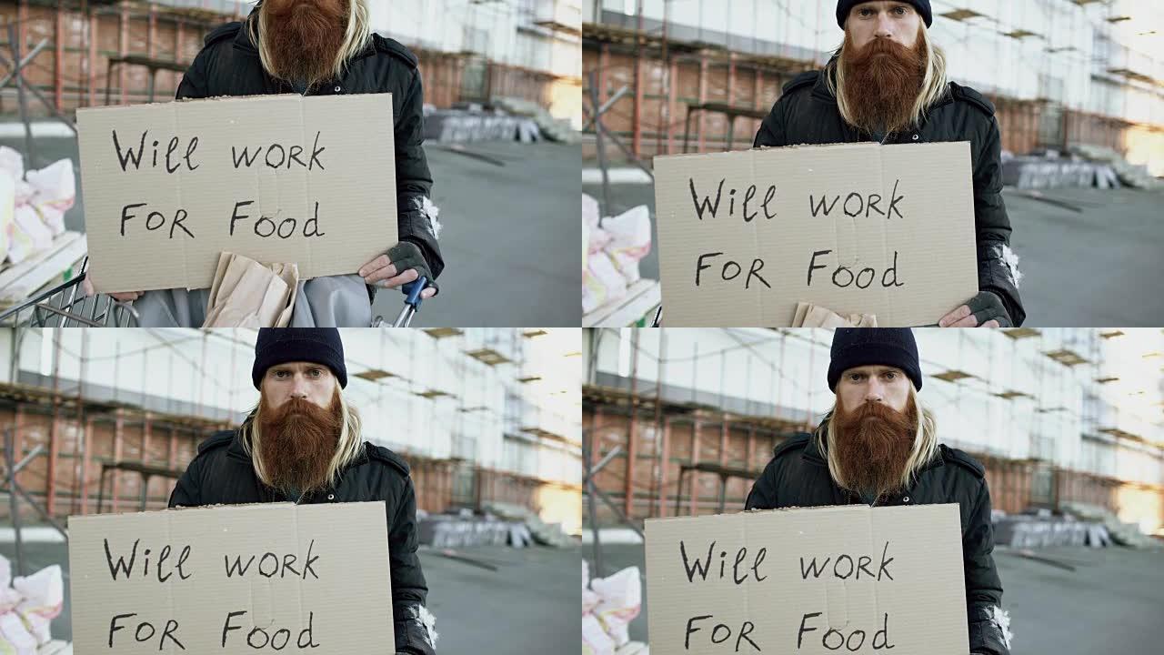 倾斜年轻无家可归者的肖像，用纸板看着相机，想为站在购物车附近的食物工作