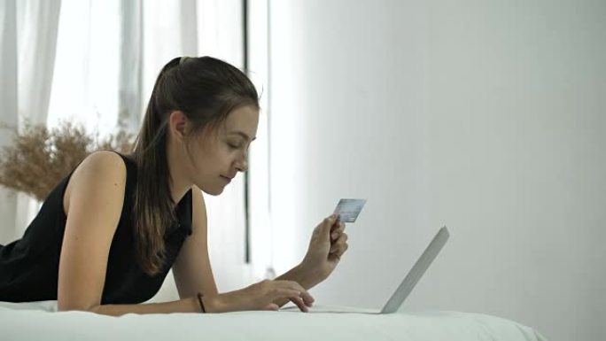 女人在卧室用信用卡在笔记本电脑上购物
