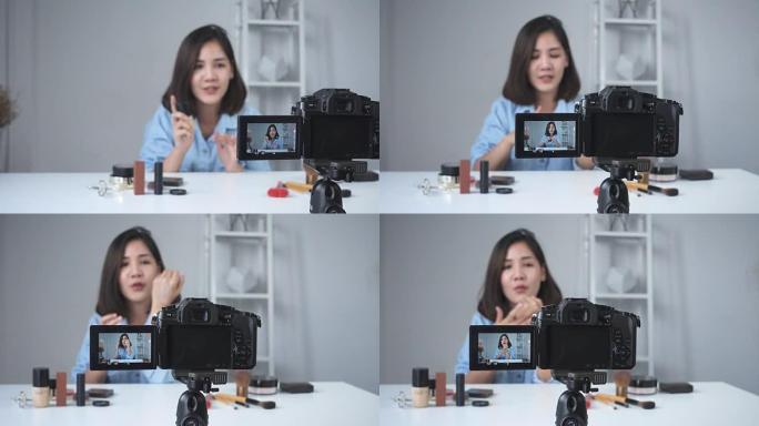 快乐微笑的亚洲女人或美容博主用刷子和相机录制视频，并在家里挥手。美女视频博客博客人物概念。多莉开枪了