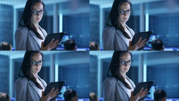 戴眼镜的年轻女性公务员在系统控制中心使用平板电脑。在后台，她的同事们在他们的工作空间里有许多显示有价