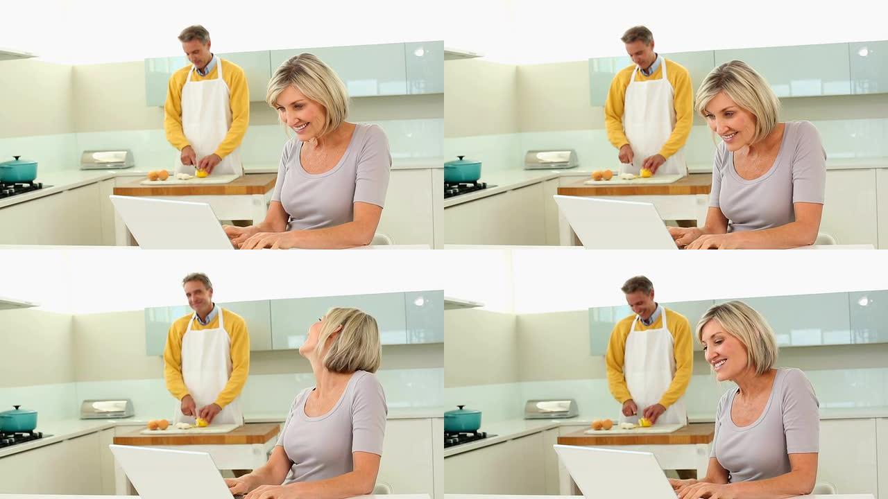 丈夫在切蔬菜时使用笔记本电脑的女人