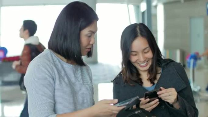 两名妇女在航站楼机场的智能手机上检查航班并在线办理登机手续