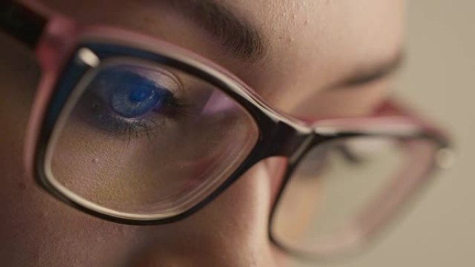 眼镜中的女人眼睛的特写镜头反映了正在工作的计算机屏幕。