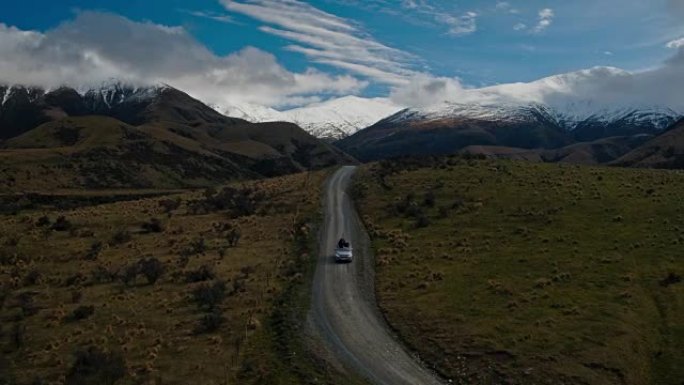 SUV在沙漠中驶向新西兰雪山山峰的鸟瞰图