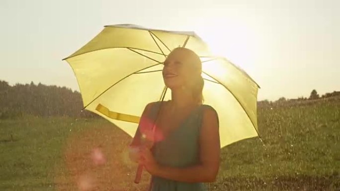 慢动作: 无忧无虑的金发女孩在她的黄色雨伞下在雨中旋转。