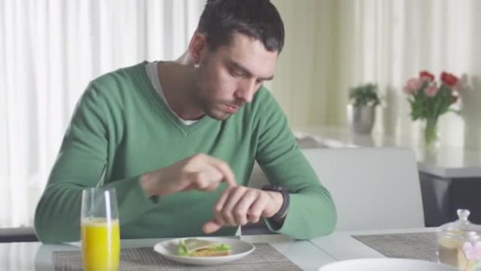 男子正在检查他的智能手表，同时在早上吃午餐和橙汁