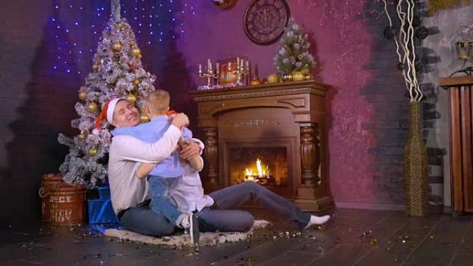 快乐的爸爸妈妈在圣诞壁炉旁拥抱他们的儿子。慢动作。