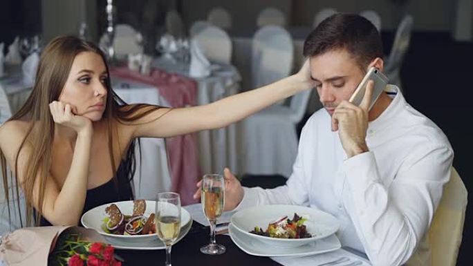 忙碌的年轻人正在用手机聊天，而他的女友坐在餐厅的餐桌旁感到无聊。现代技术、关系和无聊概念。