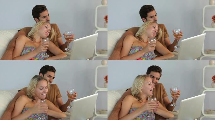 夫妇躺在沙发上看笔记本电脑喝酒