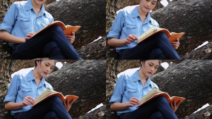 年轻迷人的女人在公园的树旁看书。