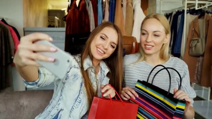 两名年轻女性在服装店购物后用智能手机自拍的特写镜头。首先，他们摆姿势并大笑，然后在屏幕上观看照片