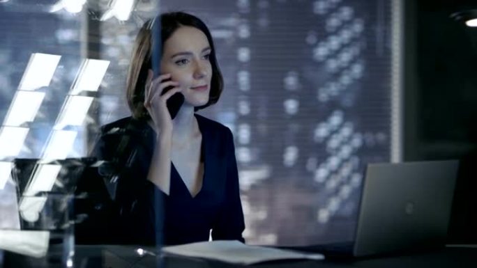 迷人的女经理坐在她私人办公室的桌子旁通过电话交谈。她身后是可以看到大城市景色的窗户。