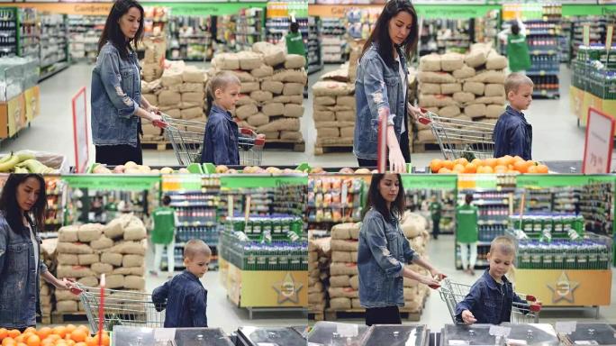 欢快的家庭妈妈和儿子在超市里用购物车选择水果和聊天的侧视图。为人父母，童年和购买食物的概念。