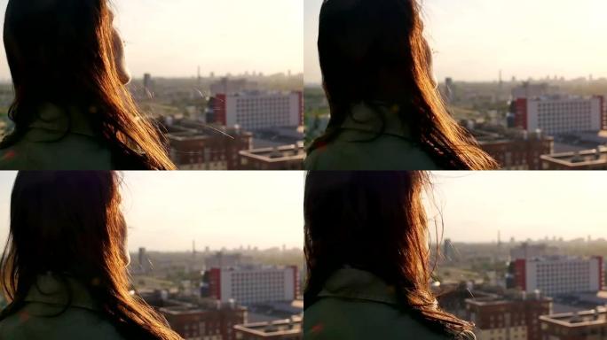 后视图。风吹起长长的黑发美丽的年轻女性。日落时站在屋顶上的女孩。慢mo
