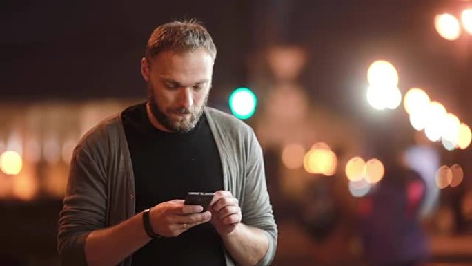 英俊的男人发短信，使用智能手机就走了。街道上模糊的城市灯光。现代技术