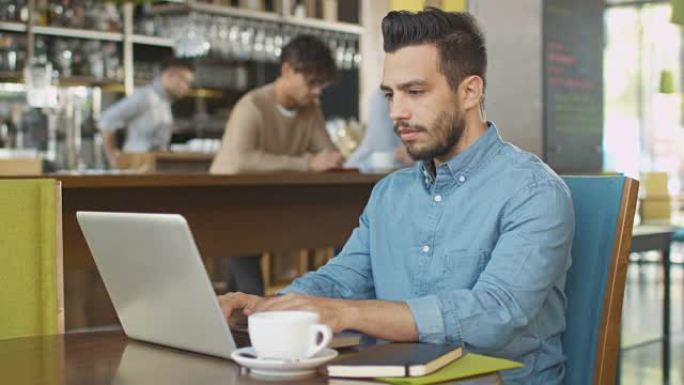 西班牙裔年轻人在舒适的咖啡店使用笔记本电脑。