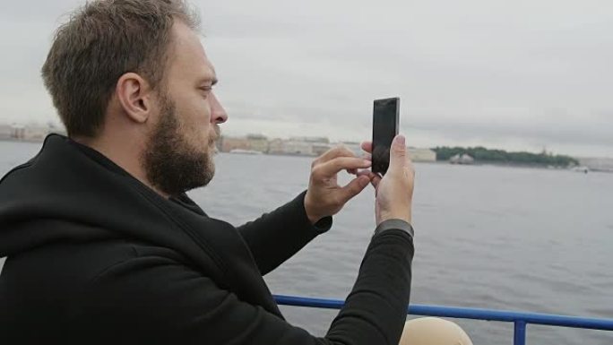 一个英俊的男人在俄罗斯圣彼得堡观光时拍照的侧景。男人使用智能手机，慢速
