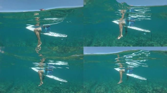 水下: 健康的男性游客坐在冲浪板上，环顾海景