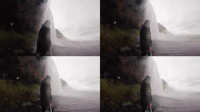 年轻的游客拿着自拍杆，在冰岛的gopro相机上拍摄强大的瀑布Seljalandsfoss