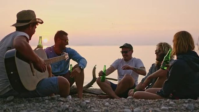 顽皮的朋友在宁静的日落海滩上喝啤酒和弹吉他