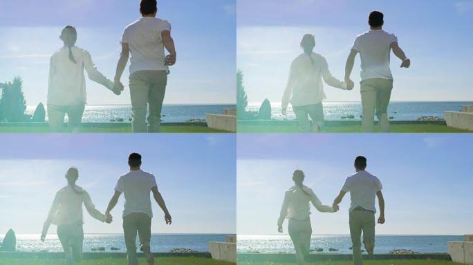 在美丽的夏日，幸福的夫妻手牵手，赤脚在草地上奔跑。在他们面前阳光明媚的蓝天和海滨景色。