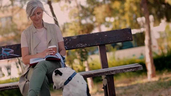 公园里有狗和咖啡阅读书的成熟女人