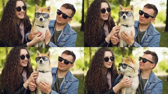 可爱的情侣帅哥和他的女朋友在亲吻血统狗，都戴着墨镜，人们在笑和触摸动物。宠物和主人的概念。