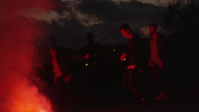 一群青少年在户外红色信号弹的灯光下闲逛跳舞。