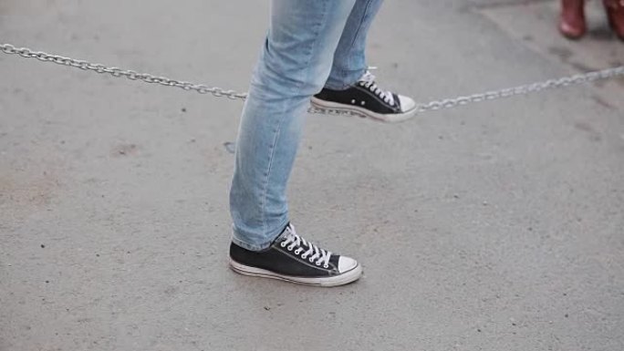 穿着运动鞋的男性腿的特写镜头。青少年在外面度过时光，触摸链条
