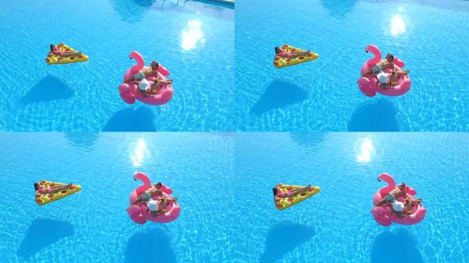 空中: 年轻人躺在游泳池里有趣的充气披萨和粉红色火烈鸟上