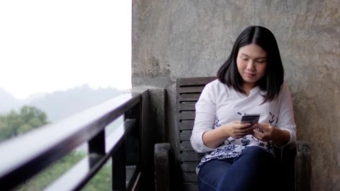 女人使用智能手机并在自然度假胜地的阳台上放松