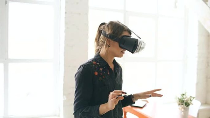 VR耳机中的女人在室内抬头并试图触摸虚拟现实中的物体
