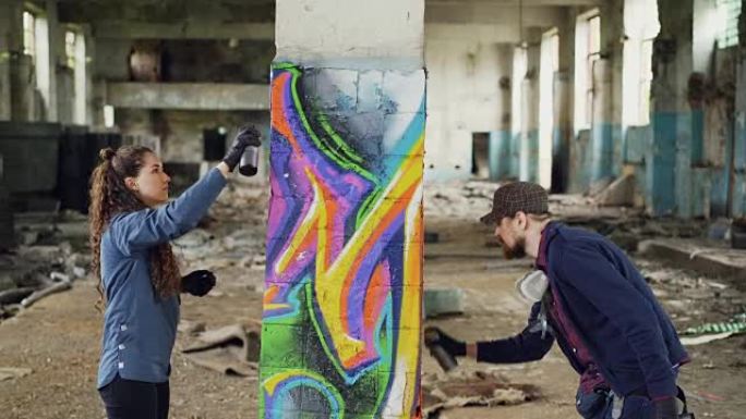 由两名城市画家组成的创意团队正在用喷漆绘制涂鸦，同时用被毁的肮脏墙壁和窗户装饰旧的工业仓库。