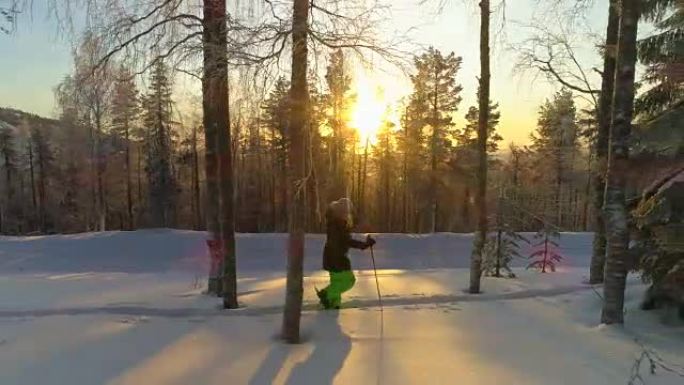 空中: 穿着冬装的女孩在金色的冬日日落时分在深雪上行走