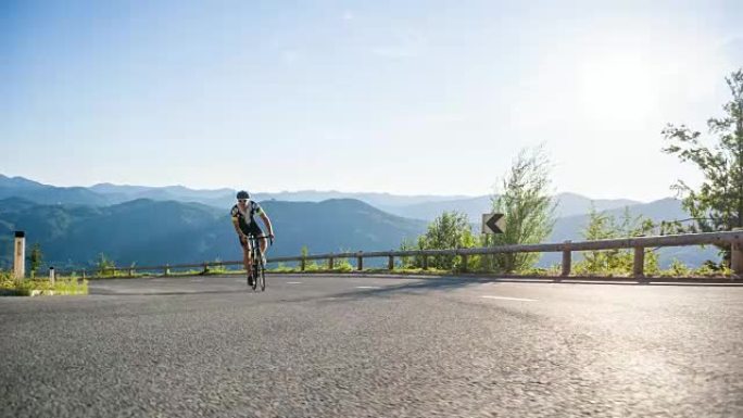 公路自行车手在背景为山脉的空旷道路上骑自行车